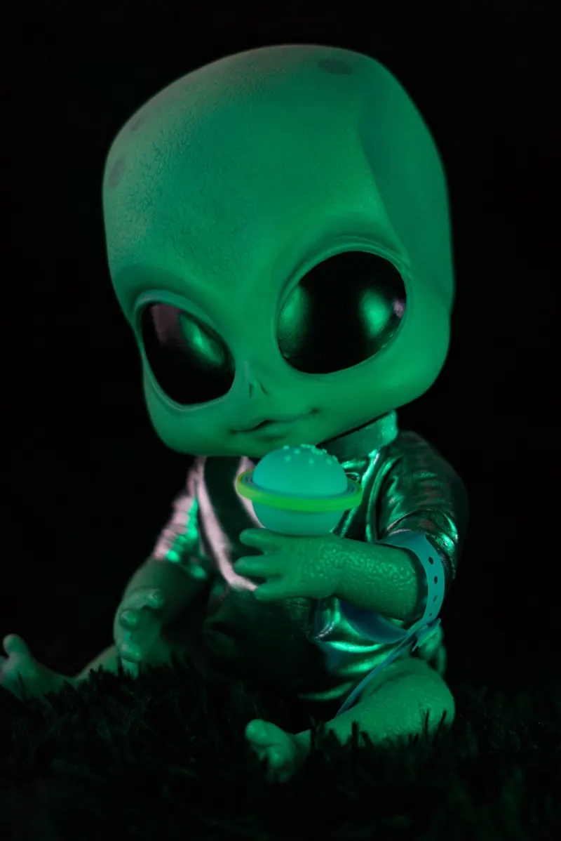 A cute alien toy with a glowing green effect, holding a futuristic device.