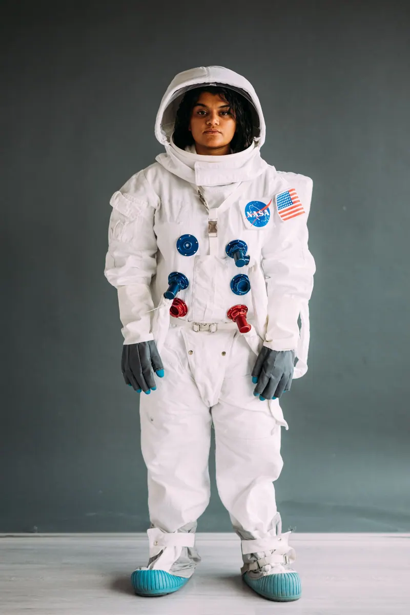 A woman stands indoors in a NASA astronaut suit, capturing a space exploration theme