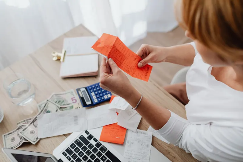 Woman using calculator and receipts at home office desk for finance management
