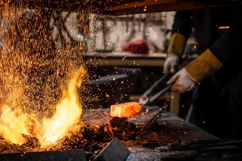 Blacksmith working with hot metal in fiery forge, sparks flying