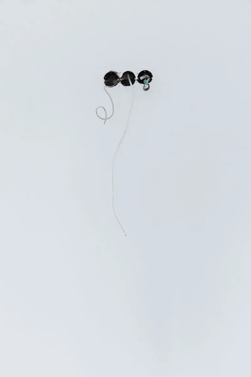 Close-up of wires emerging from holes in a white wall, showcasing electrical installation