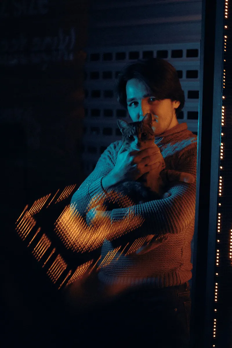 A man holding a cat, bathed in dramatic neon light, creating a moody, urban atmosphere
