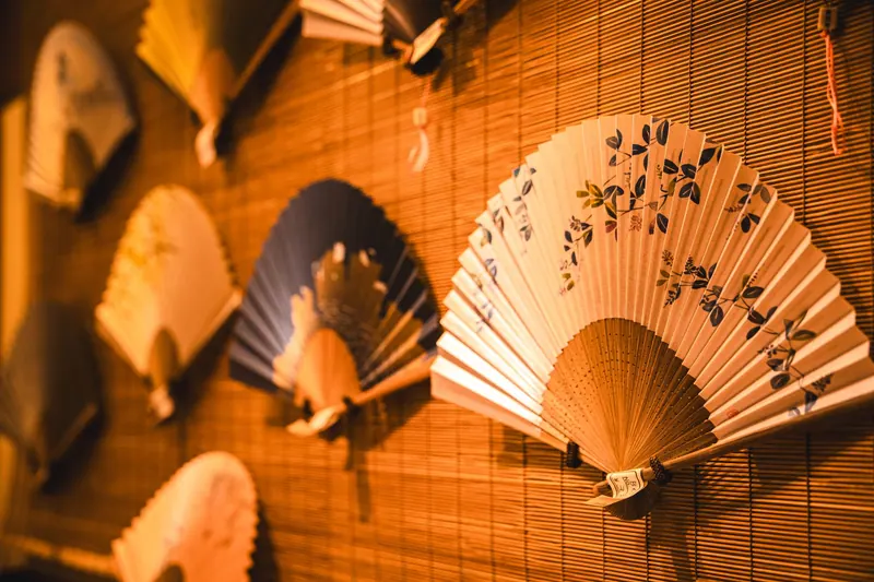 A display of traditional Japanese paper fans with intricate designs mounted on a bamboo wall