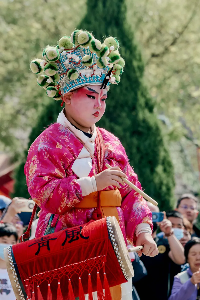 A young performer dressed in vibrant traditional Chinese festival attire with a drum