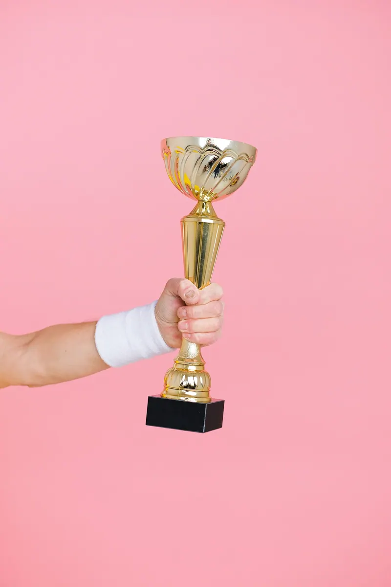 Hand raising a golden trophy against a bright backdrop