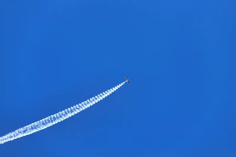 An airplane creates a dramatic contrail against a vivid blue sky, showcasing aerial acrobatics