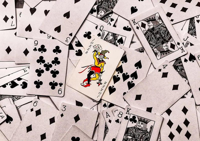 A vibrant joker card standing out in a scattered deck of monochrome playing cards