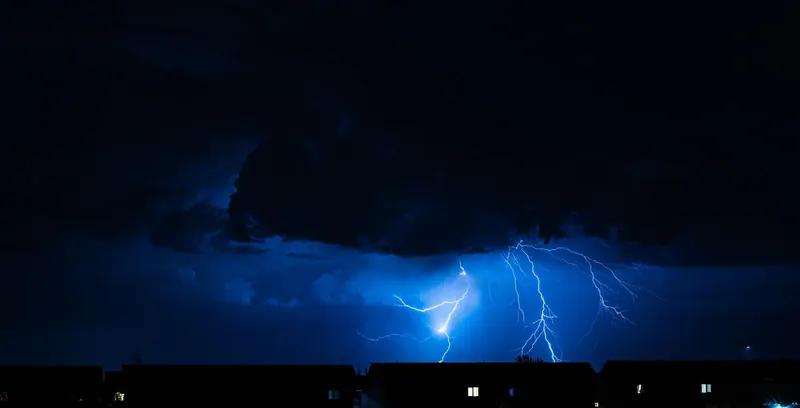 Powerful lightning illuminates the night sky during a storm, casting silhouettes over city rooftops