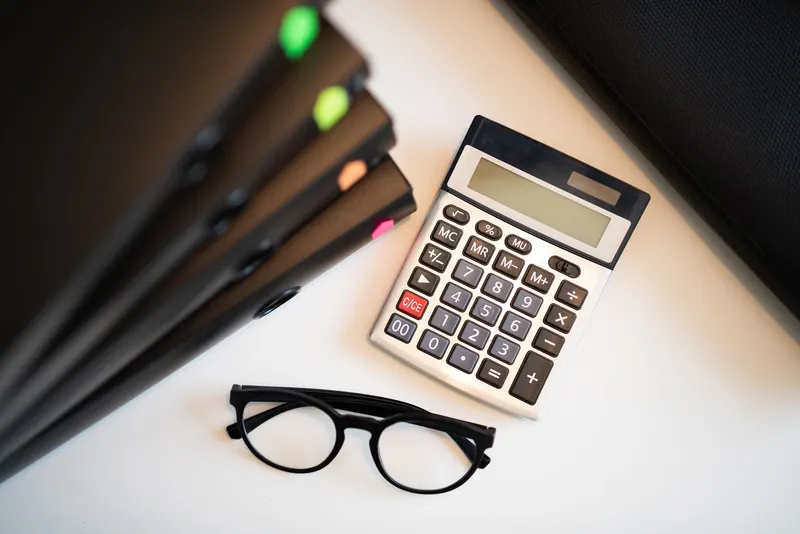 A white calculator beside eyeglasses on a desk