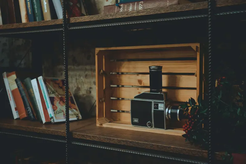 A vintage camera displayed on a wooden shelf among books, evoking nostalgia in a cozy library environment