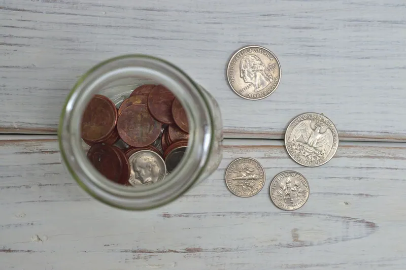 A jar filled with coins on a wooden table, seen from above