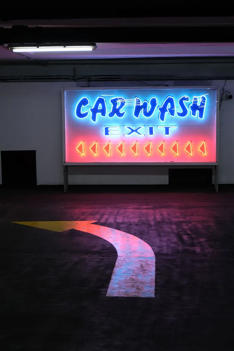 Neon car wash exit sign with directional arrow in an indoor parking area
