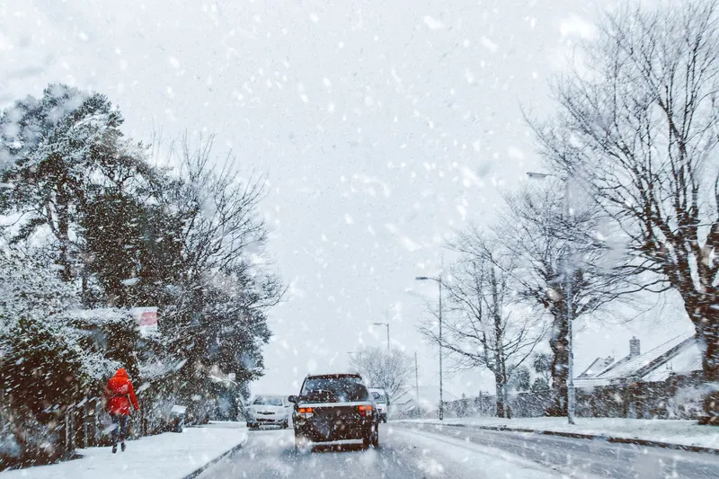 A car driving through a snowy road during a heavy winter storm, capturing a serene winter landscape