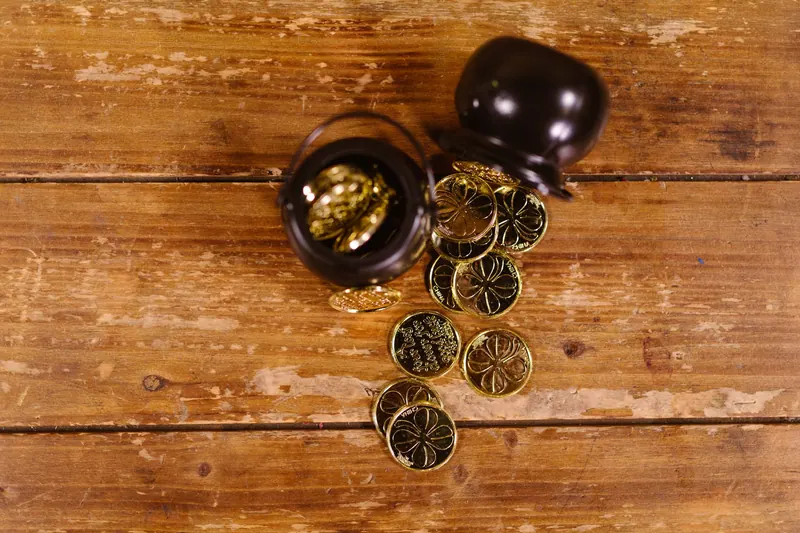 A top-down shot of gold coins spilling from a pot onto a rustic wooden table, symbolizing luck and prosperity