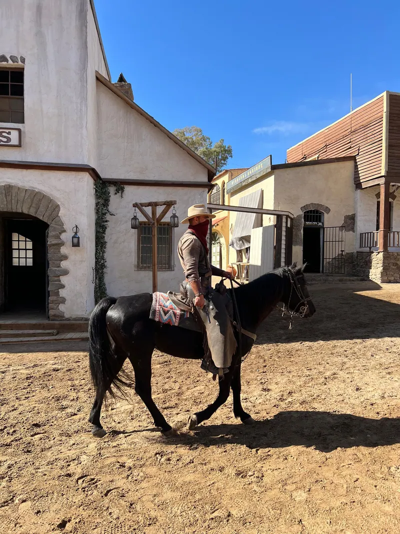 Cowboy in traditional attire rides black horse through historic Western town