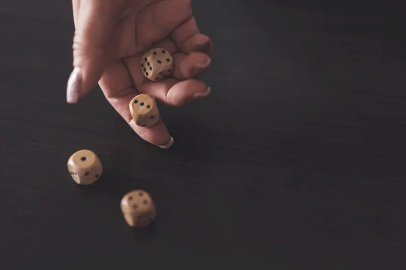 A hand rolling wooden dice across a dark wooden table
